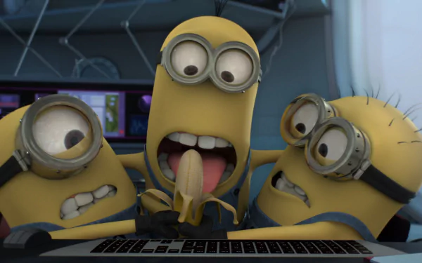 Three animated Minions from Despicable Me 2 gather around a laptop, with one excitedly holding a banana. This vibrant HD wallpaper captures their playful energy.