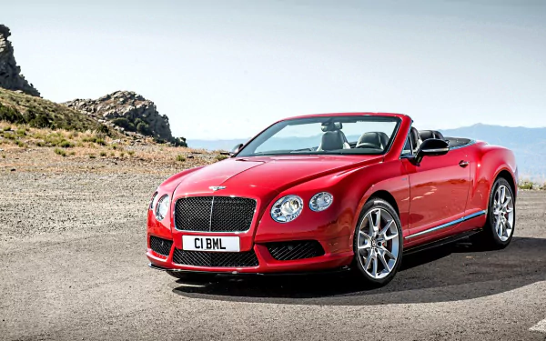 A red Bentley Continental GT V8 convertible parked on an open road with rocky terrain and clear skies, displayed as an HD PC desktop wallpaper.