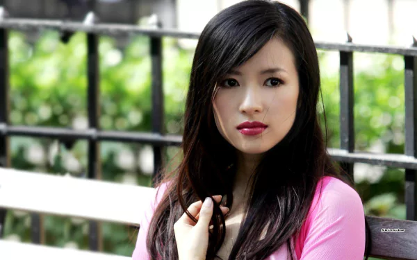A captivating portrait of the celebrity Zhang Ziyi, featuring her in a pink top with lush greenery in the background, making for a striking HD desktop wallpaper.