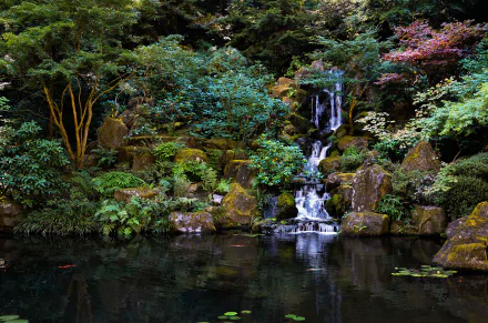 A serene Japanese garden featuring a tranquil pond and a cascading waterfall, surrounded by lush greenery and vibrant foliage, creating a peaceful natural atmosphere.