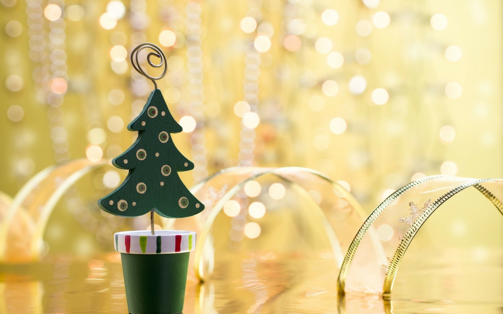 A decorative green Christmas tree in a pot stands against a shimmering golden background, creating a festive atmosphere for holiday-themed HD desktop wallpaper.