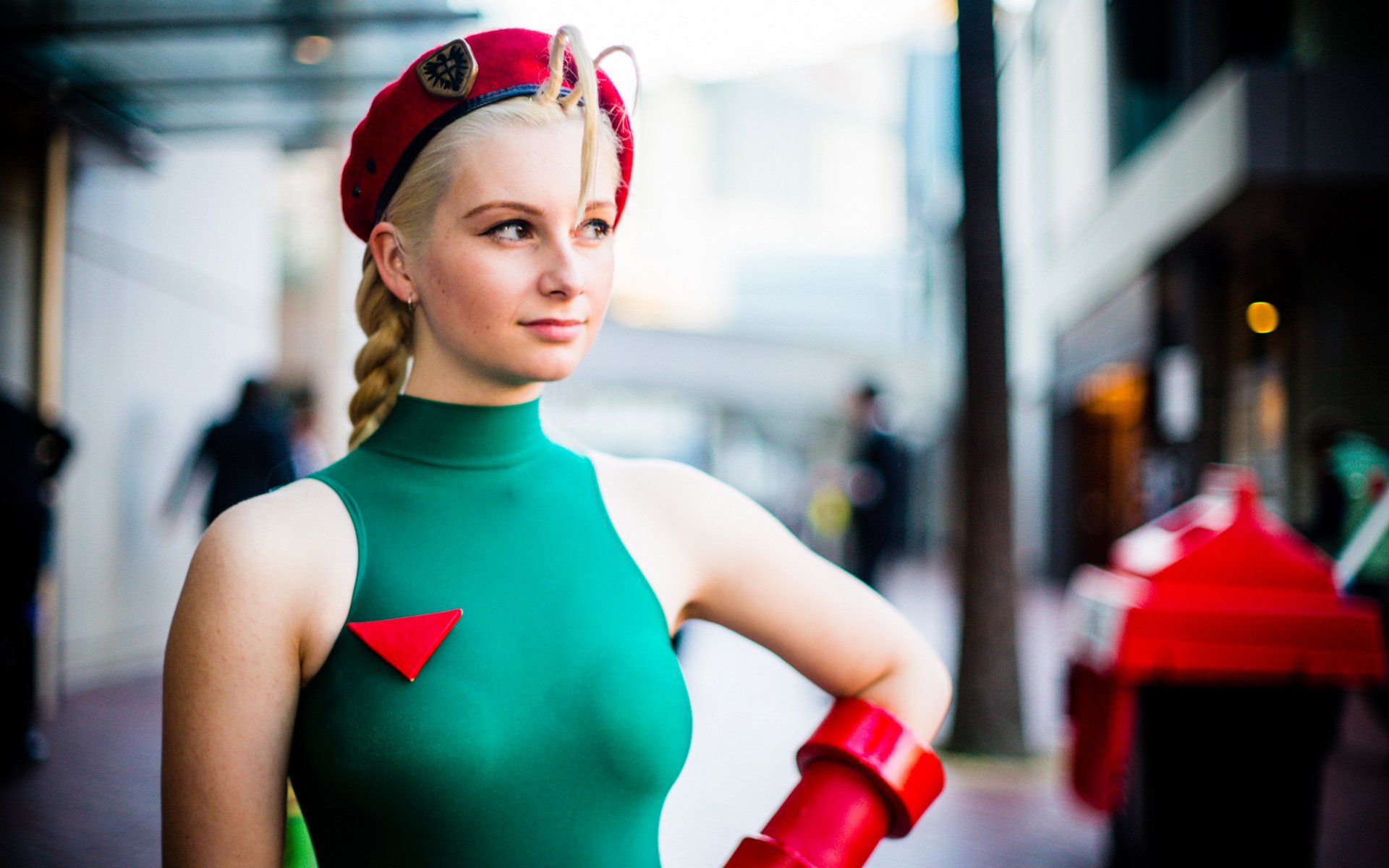 A woman in vibrant cosplay attire poses confidently, showcasing a striking green costume and red accessories. This HD image serves as an engaging desktop wallpaper or background.
