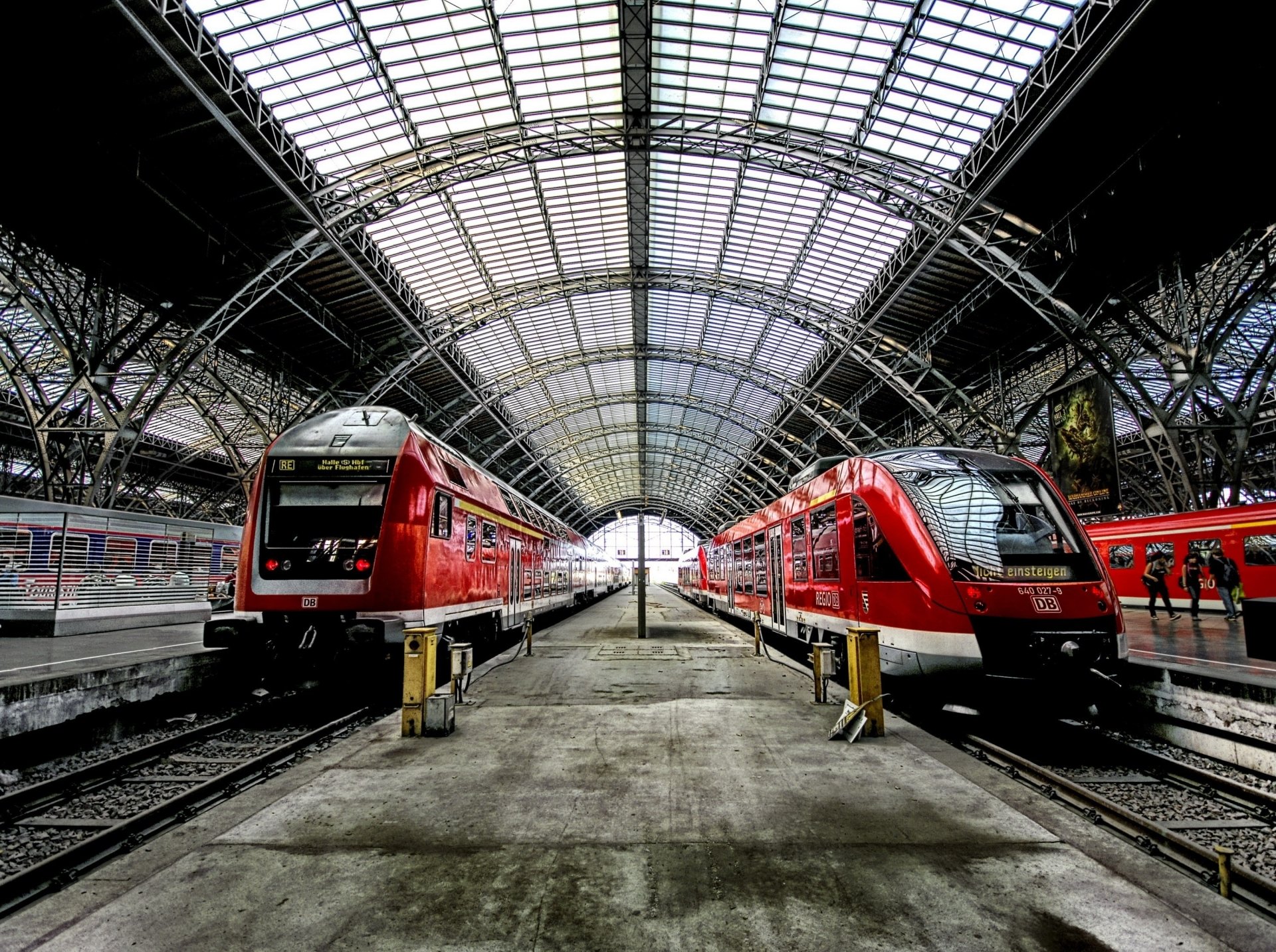 HD desktop wallpaper featuring a train station in Germany with two red trains facing each other under a large arched metal and glass roof.