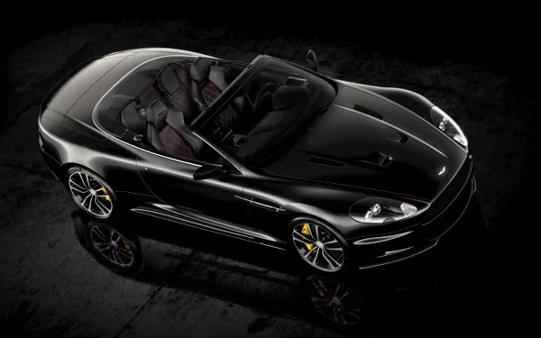 Sleek black Aston Martin DBS convertible captured in high definition, showcasing its elegant design and luxurious interior against a dark background.