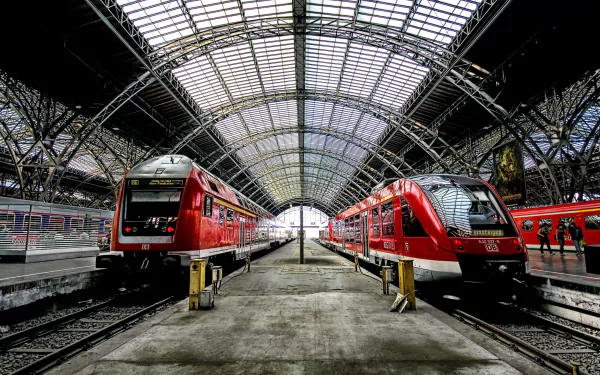 HD desktop wallpaper featuring a train station in Germany with two red trains facing each other under a large arched metal and glass roof.