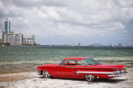 A vibrant vintage Chevrolet Impala parked by the shore, with a scenic view of the city skyline and ocean in the background, creating a stunning HD desktop wallpaper.