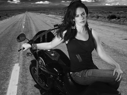 Maggie Siff sitting on a motorcycle on a deserted road, in a promotional wallpaper for the TV show Sons of Anarchy.