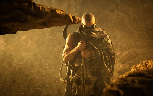Riddick from the movie standing cloaked and armed in a rain-swept rocky cave — 2K Quad HD PC desktop wallpaper/background.