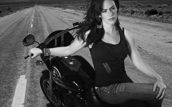 Maggie Siff sitting on a motorcycle on a deserted road, in a promotional wallpaper for the TV show Sons of Anarchy.