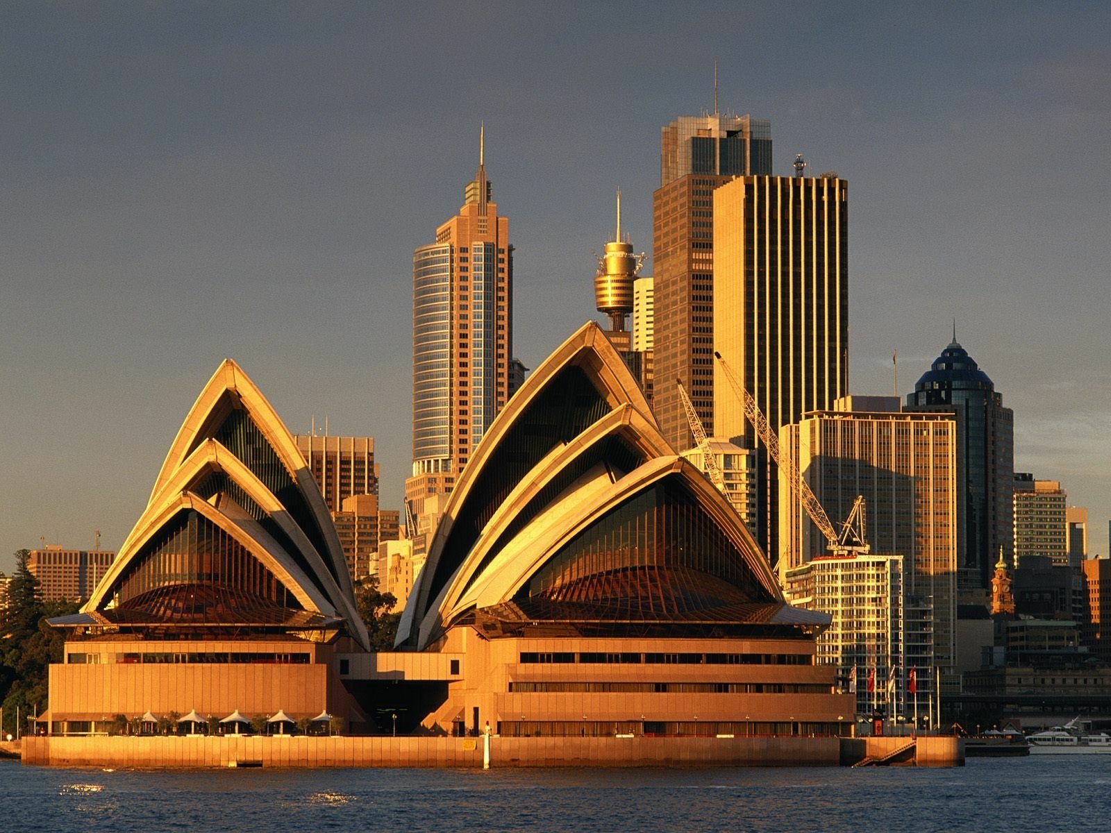 HD desktop wallpaper showcasing the Sydney Opera House with city skyscrapers in the background, highlighting iconic man-made architecture in Sydney at golden hour.