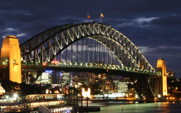 Night view of the illuminated Sydney Harbour Bridge in Australia, showcasing the city skyline and waters beneath in this HD desktop wallpaper.