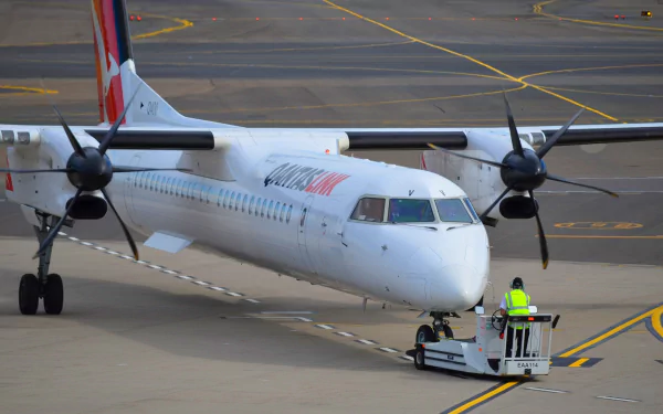 Passenger Qantas Bombardier Dash 8 aircraft at airport tarmac, with ground crew in high-visibility jacket guiding the vehicle, captured in HD quality.