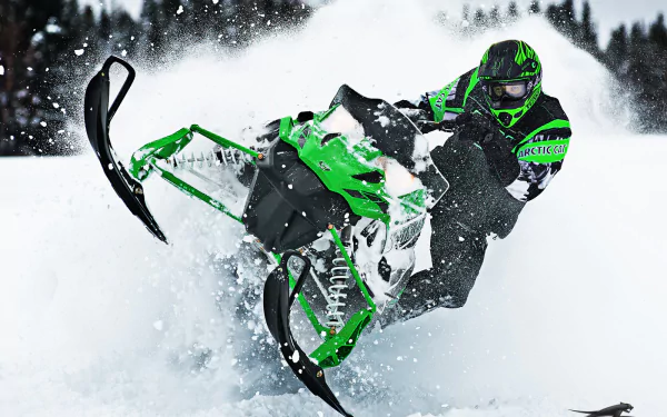 HD PC desktop wallpaper of a green snowmobile vehicle carving through deep powder, rider leaning sharply as snow sprays, with a blurred pine forest in the background.