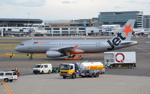 A Jetstar Airbus A320 is seen on the tarmac at an airport, with refueling vehicles nearby, highlighting airport operations and aircraft servicing.
