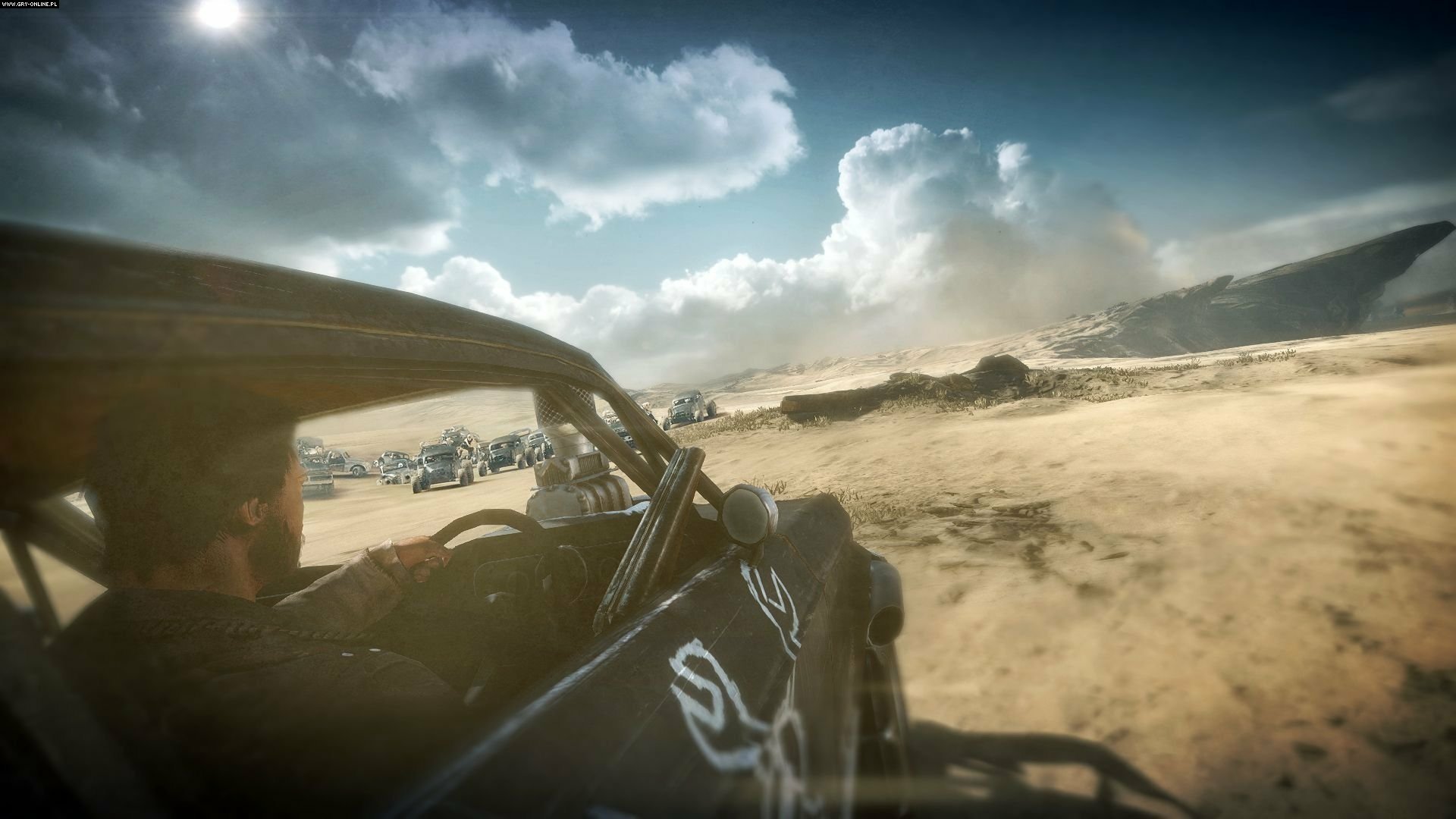 HD PC desktop wallpaper of the Mad Max video game: first-person dune-buggy view racing across a sunlit desert, kicking up dust under dramatic clouds and distant wreckage.