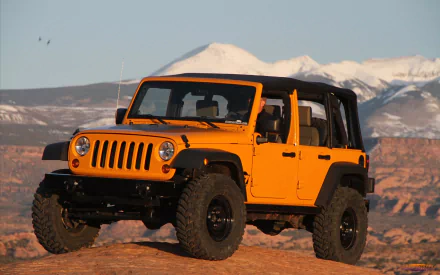 A vibrant orange Jeep parked on rocky terrain, with snow-capped mountains in the background, creating a stunning HD desktop wallpaper.