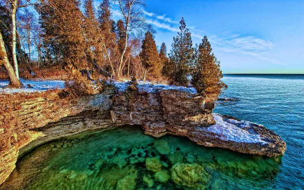 HD PC desktop wallpaper and background of Lake Michigan shore: rocky limestone coastline with trees and dusting of snow over clear green-blue water and exposed shallow ledges.