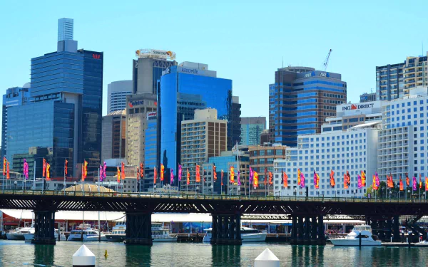 Pyrmont Bridge, a man-made span across Darling Harbour in Sydney, Australia, with colorful flags and modern city buildings under a clear blue sky.