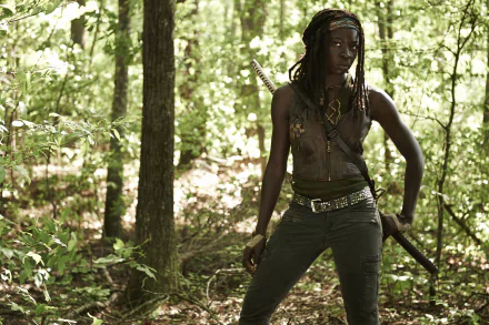 HD wallpaper featuring Michonne from The Walking Dead, portrayed by Danai Gurira, standing confidently in a lush, green forest with a sword.