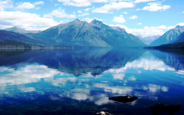 Serene Lake McDonald landscape with calm waters reflecting clouds and mountain peaks, captured in vivid HD for a stunning nature desktop wallpaper.