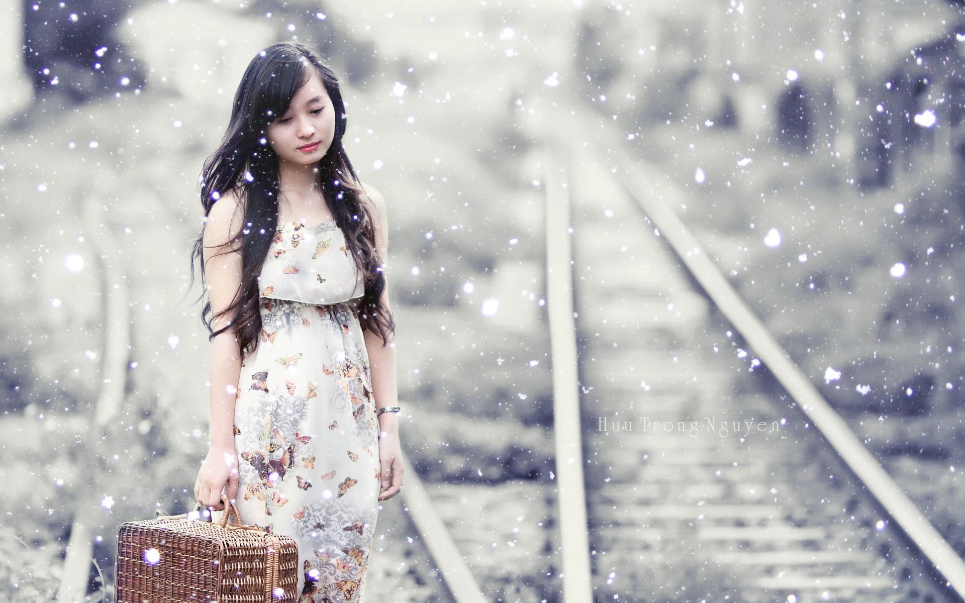 HD wallpaper of an Asian woman walking on train tracks, carrying a suitcase, amidst falling snow.