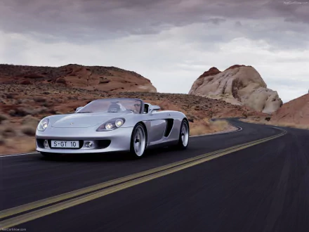 A sleek Porsche Carrera GT drives along a winding road, surrounded by stunning rock formations, creating an impressive HD desktop wallpaper for car enthusiasts.