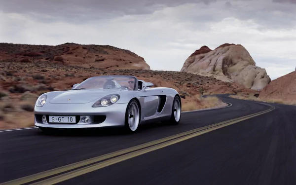 A sleek Porsche Carrera GT drives along a winding road, surrounded by stunning rock formations, creating an impressive HD desktop wallpaper for car enthusiasts.
