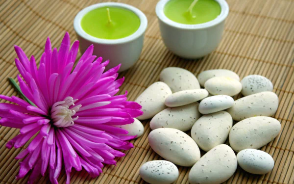 HD desktop wallpaper featuring a man-made spa setting with a vibrant purple flower, smooth white stones, and two green candles on a bamboo mat.