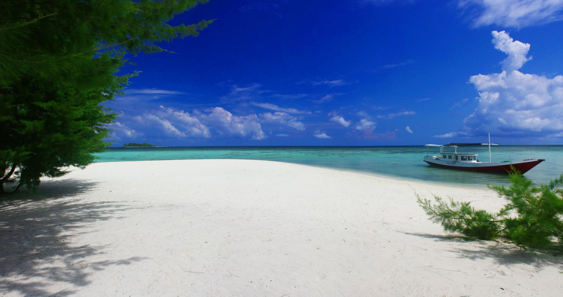 4K Ultra HD desktop wallpaper featuring a serene beach with white sand, clear turquoise water, a boat anchored near the shore, and a bright blue sky with scattered clouds.