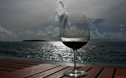 HD wallpaper featuring a glass of wine on a wooden table with a sparkling sea and distant island backdrop.
