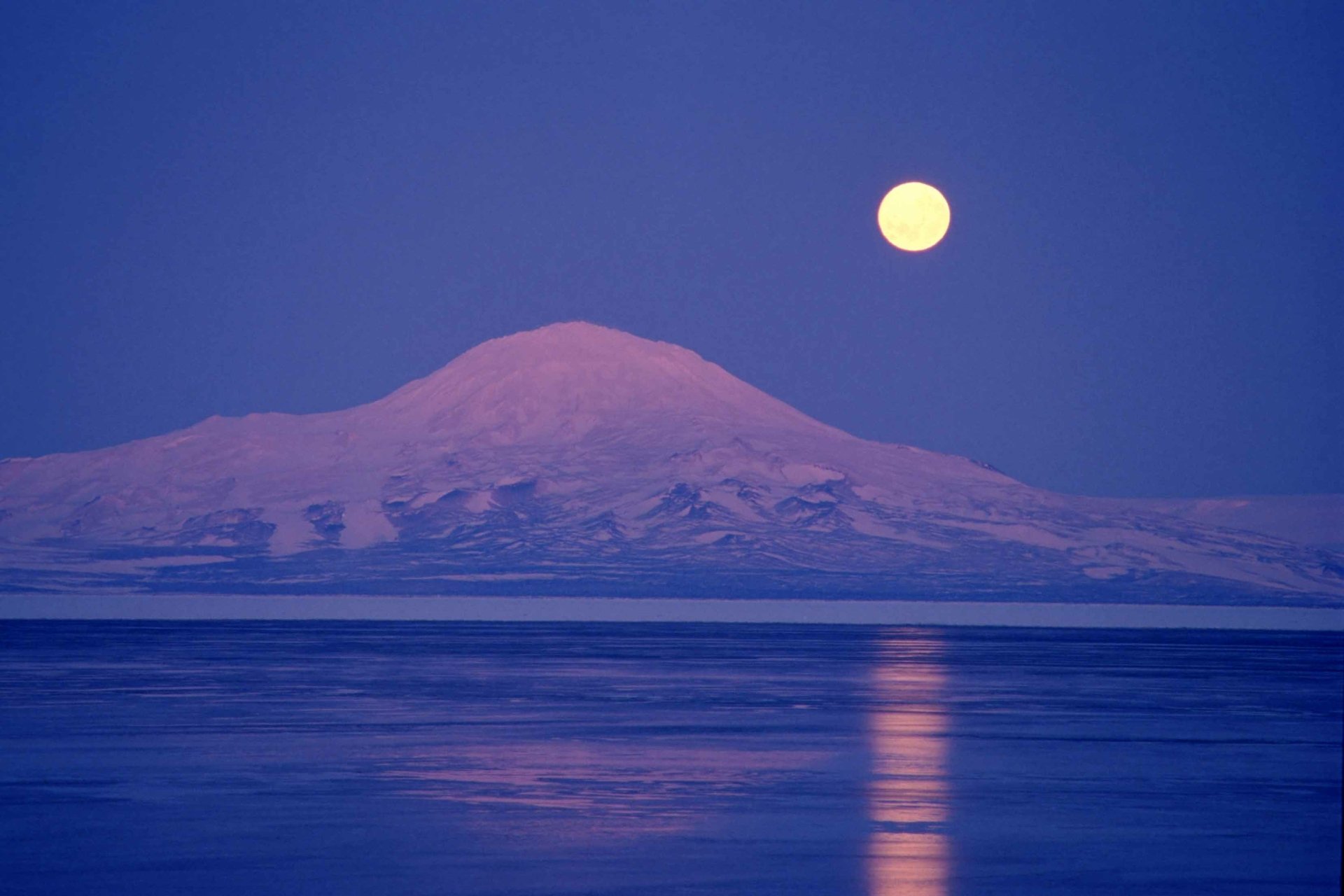 A serene HD nature image featuring a full moon illuminating a snow-capped mountain, reflected in tranquil waters, creating a calming background for any desktop.