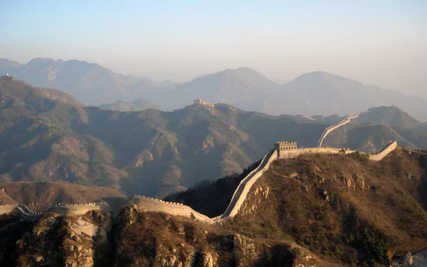 The Great Wall of China stretches majestically over rugged mountains, showcasing a remarkable feat of human engineering against a serene, hazy backdrop. HD desktop wallpaper.