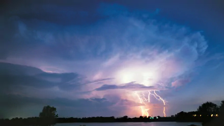 A striking HD desktop wallpaper featuring a dramatic lightning storm illuminating dark clouds over a tranquil landscape, showcasing the power of nature.