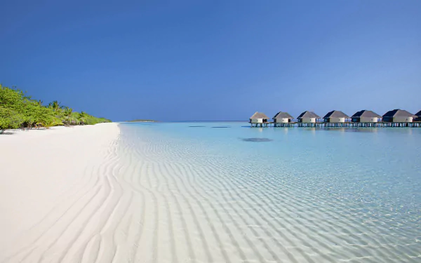 HD PC desktop wallpaper featuring serene beach with clear water, white sand, and a row of huts extending over the ocean under a clear blue sky.