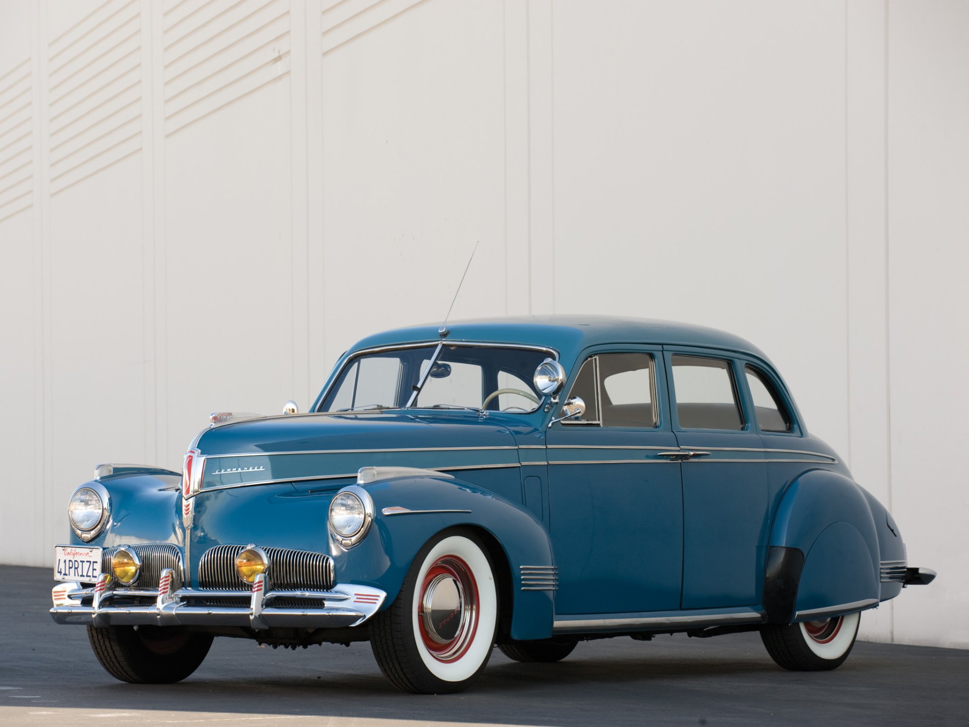 Blue Studebaker sedan parked before a pale wall — HD PC desktop wallpaper and background featuring a classic vehicle.