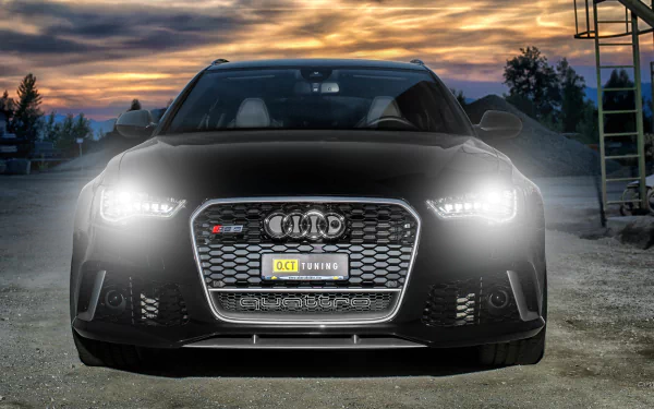 HD PC desktop wallpaper featuring a sleek black Audi RS6 with headlights on, set against a dramatic sunset sky and industrial background.