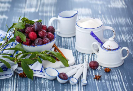 HD desktop wallpaper featuring fresh plums in a white bowl alongside white ceramic kitchenware with blue accents on a textured blue surface.