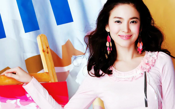 A vibrant HD desktop wallpaper featuring Korean celebrity Song Hye Kyo smiling, adorned with colorful earrings, against a backdrop of artistic elements.