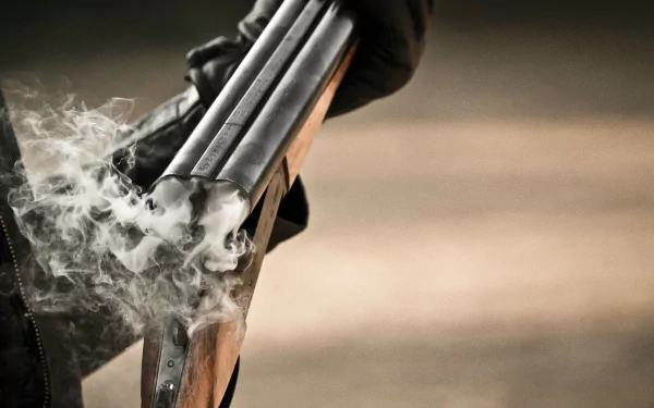 HD desktop wallpaper showing a close-up of a man-made shotgun being fired, with smoke rising from the barrels against a blurred background.