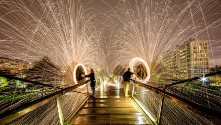 A striking image of fire juggling on a wooden bridge, showcasing vibrant sparks and dynamic light trails against a nighttime city backdrop. A stunning 4K Ultra HD desktop wallpaper.