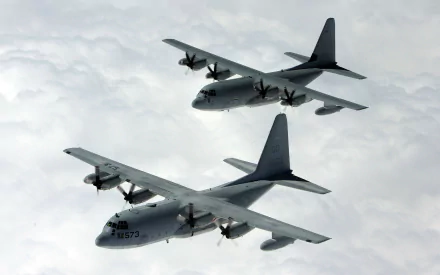 Two Lockheed C-130 Hercules military transport aircraft fly in formation above the clouds in this HD desktop wallpaper and background image.
