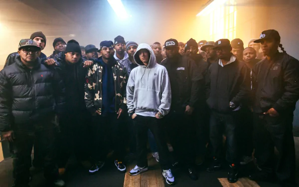 HD wallpaper featuring Eminem standing with a large group of people in a dimly lit setting, tagged with music.