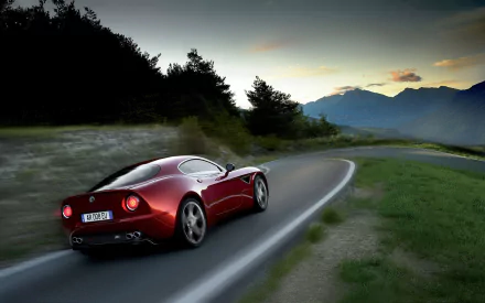 HD PC desktop wallpaper of a red Alfa Romeo 8C Competizione vehicle driving along a winding mountain road at dusk.
