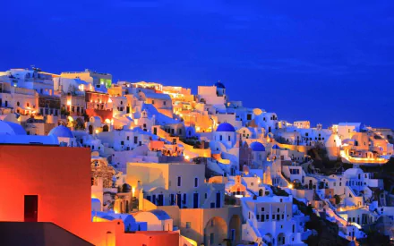 A stunning view of Santorini at night, showcasing its iconic white buildings illuminated against a deep blue sky, creating a captivating man-made landscape.