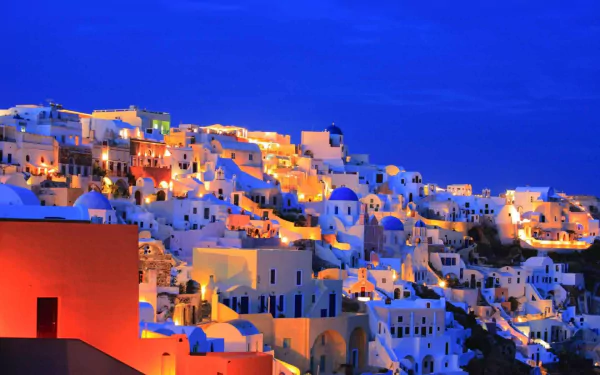 A stunning view of Santorini at night, showcasing its iconic white buildings illuminated against a deep blue sky, creating a captivating man-made landscape.
