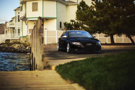 A sleek Audi A4 parked by a waterfront, framed by lush greenery and modern homes, creates a captivating HD desktop wallpaper and background.