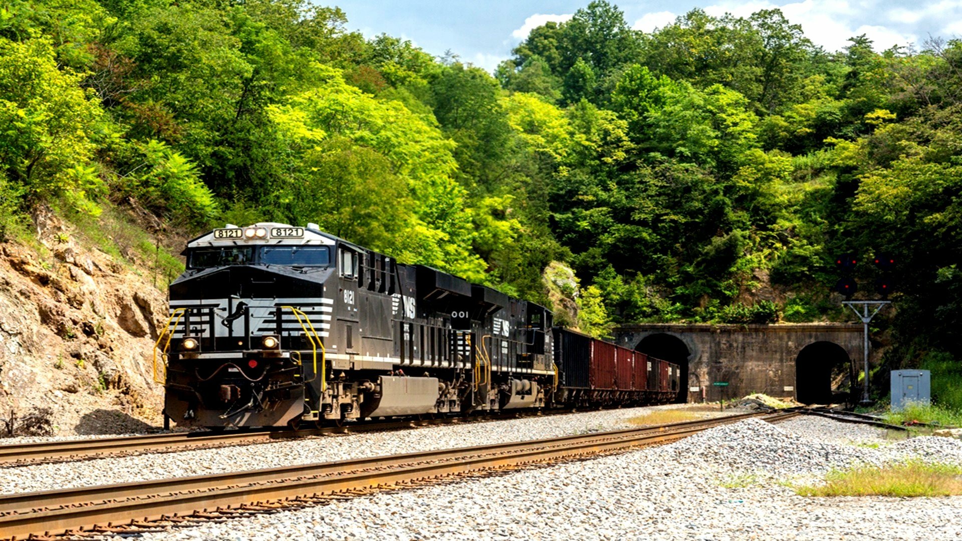 HD PC desktop wallpaper featuring a black freight train emerging from a tunnel surrounded by lush green trees under a clear sky.