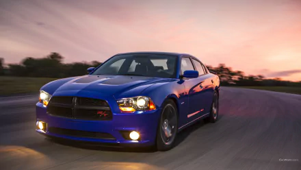 HD desktop wallpaper featuring a blue Dodge Charger Daytona driving on a curved road at sunset.