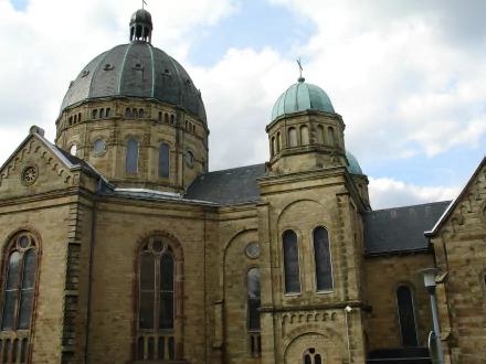 Basilique Notre-Dame de Saint-Avold: stone church with domes and arched windows against a cloudy sky — 2K Quad HD PC desktop wallpaper.