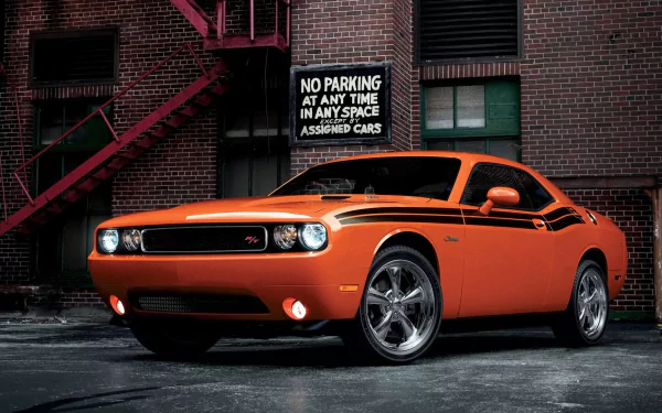 HD PC desktop wallpaper: orange Dodge Challenger RT muscle car parked by a brick building, glossy finish and chrome wheels — bold vehicle background